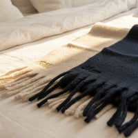 Load image into Gallery viewer, Chunky Tassel scarves in Black and Beige, on a bed. Both have personalised embroidered letters on them
