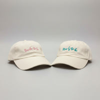 Load image into Gallery viewer, two beige caps with Mrs G to Be embroidered on the front of one, and Bride to Be embroidered on the other.

